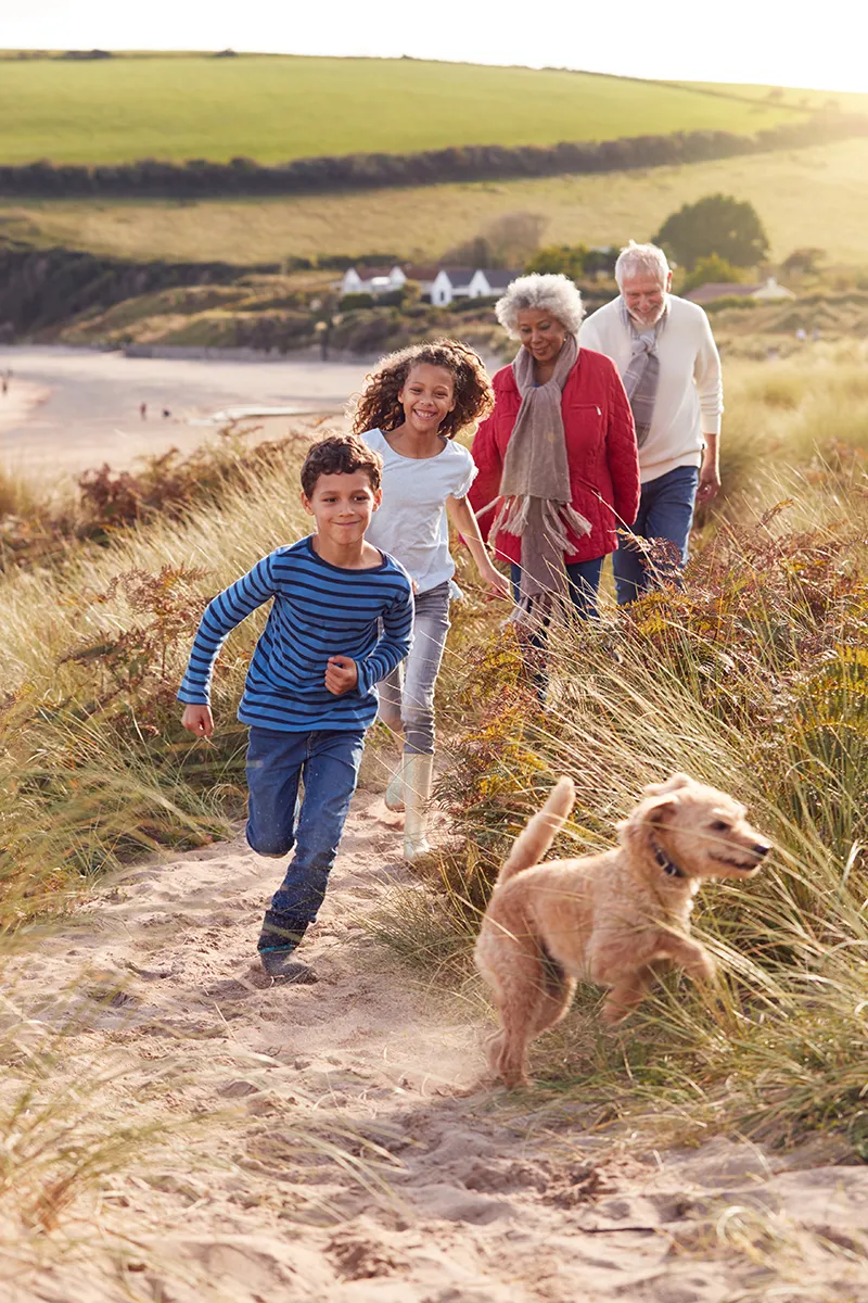 local-medicare-agents-az-active-senior-family A happy multi-generational family walks along a sandy coastal path with a golden dog, representing the active, worry-free retirement that comes with trusted Medicare coverage in Arizona.